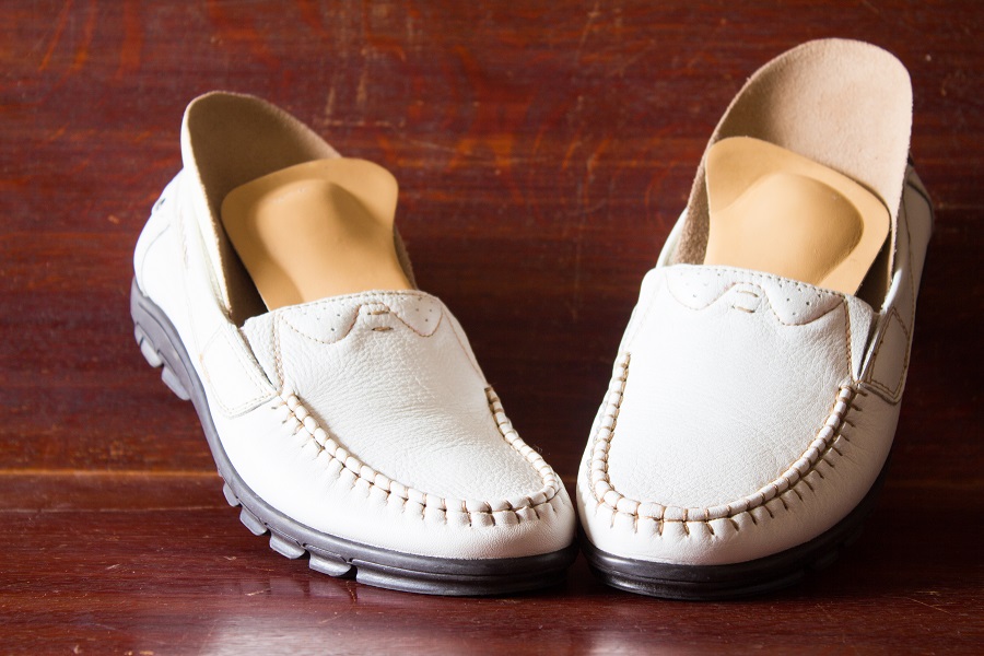 Weiße Damenschuhe mit verschiedenen orthopädischen Einlagen sind auf dem Boden platziert.